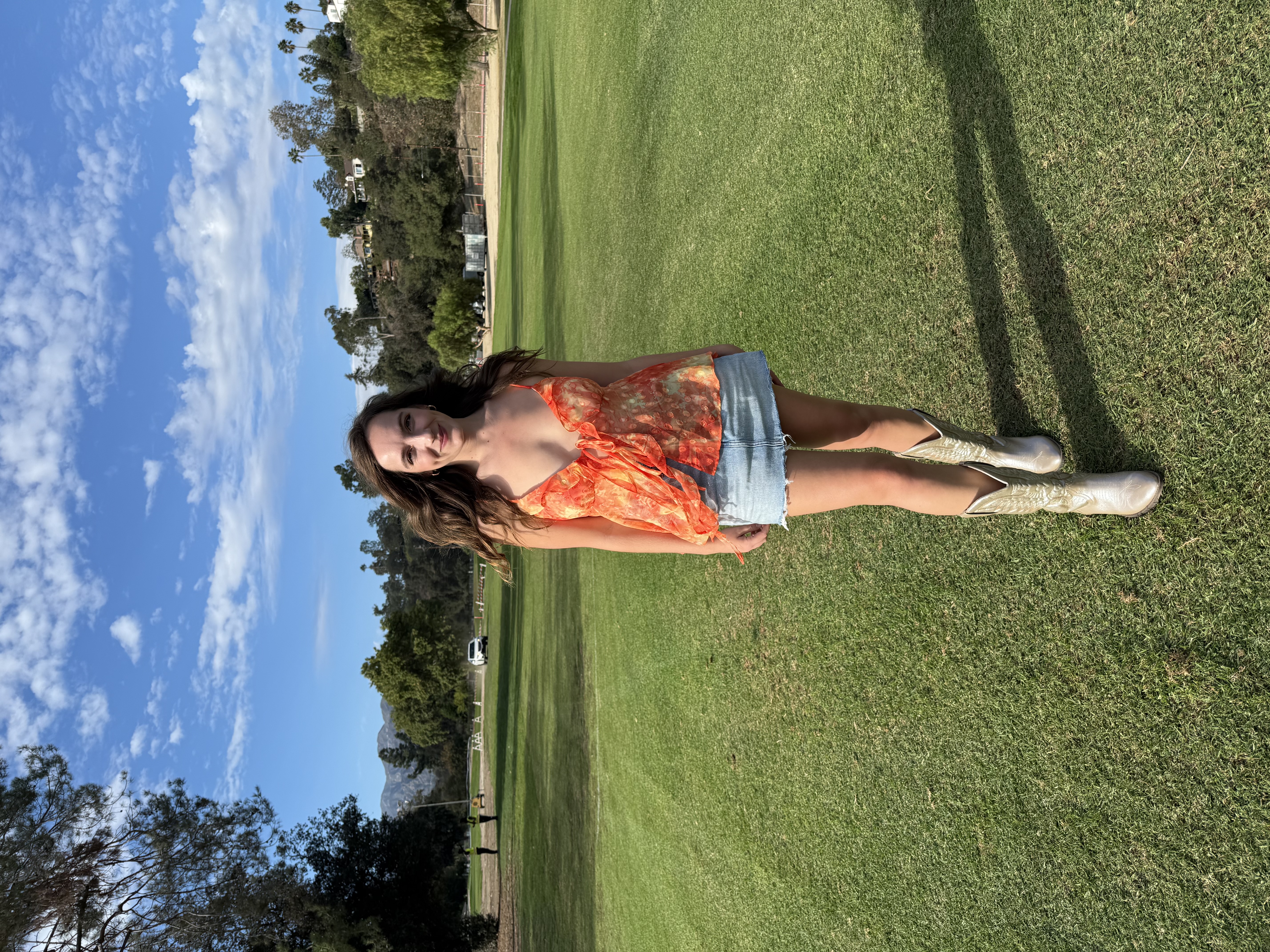 Full body shot of Emily wearing the Jaya Top with jeans and white shoes at a park